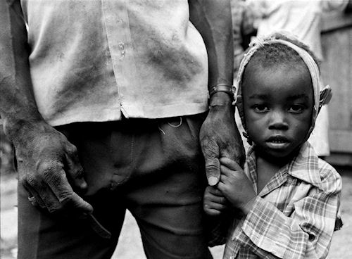 There was a tiny hamlet, maybe six hours outside Port au Prince, filled with the ghosts of small children. The whole area, not just the village, had been isolated by the Cedras regime, and now three-quarters of the town's children had died in a mumps epidemic. Their parents had voted for Aristide in the previous election, and those votes -- officially registered in Port au Prince -- had cost them dearly under the current military dictatorship. Add the U.S. embargo, and the people were virtually cut off from the capitol. The village leader had lost three children of his own; two in one day, and a third he had carried on his back all the way down a long, treacherous road to a health clinic that had been closed. The military, weeks before, had cleared out all medicine and equipment and taken it back to Port au Prince -- more punishment for their Aristide vote. He made the long trek back to his village -- with child on his back -- where she later died. Now his son -- his last child -- was sick. This portrait shows this child clutching the hand of his father. My eyes locked with the village leader for quite some time and knew what he said was very important. I asked my interpreter what he said and his response was, 'please tell the world we are the ones who are suffering.' Photo copyright ©2010, Colin Finlay. Photo and caption provided by Western Digital Corp. Click for a bigger picture!